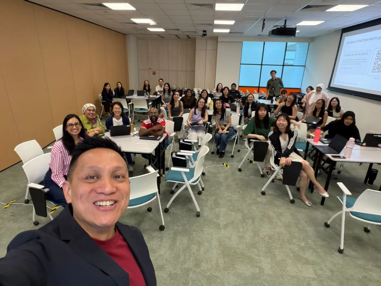 Roy Tan taking a selfie with MOM's communications teams, seated at tables with laptops